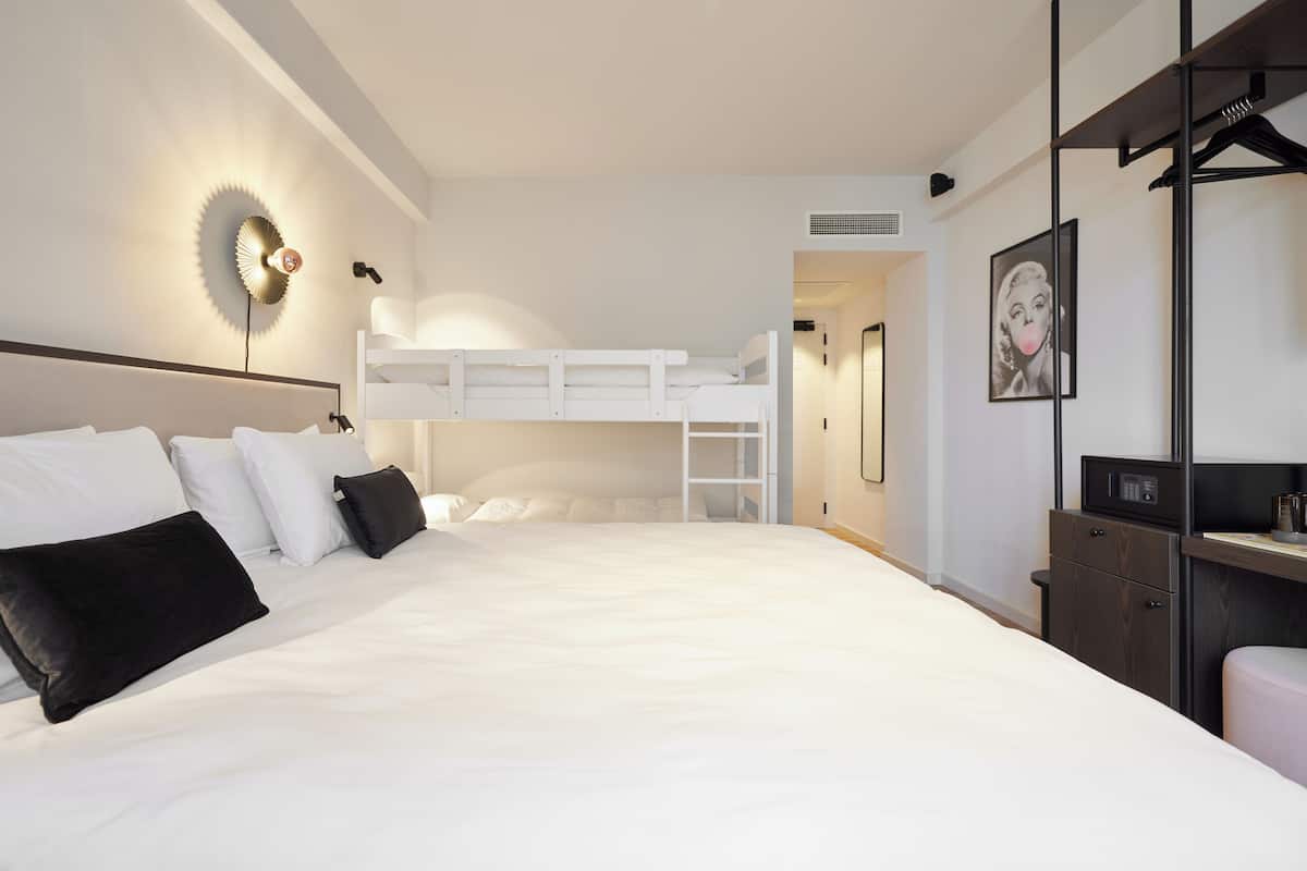 A modern hotel room with a bunk bed, a desk, and a wardrobe.