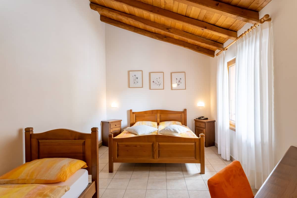 Quarto com cama de madeira, duas mesas de cabeceira, um criado-mudo e uma janela com cortinas.