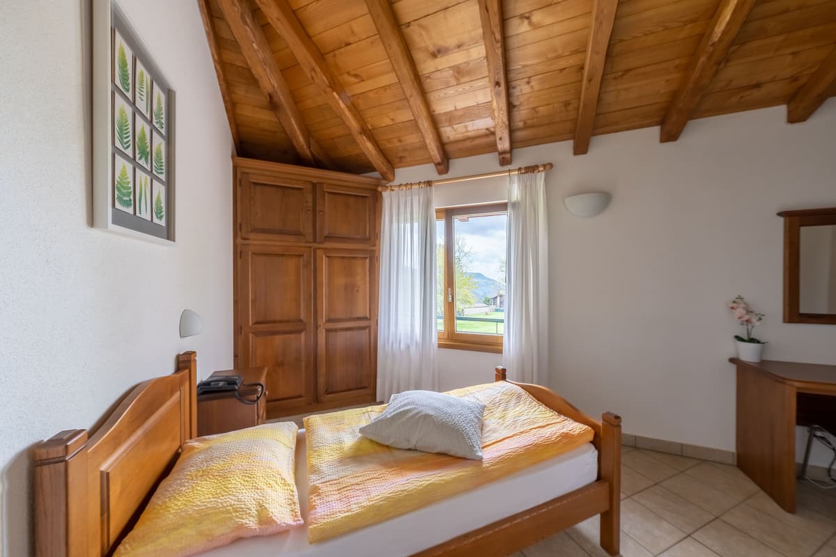 Quarto com cama de madeira, uma escrivaninha e janela com cortinas.
