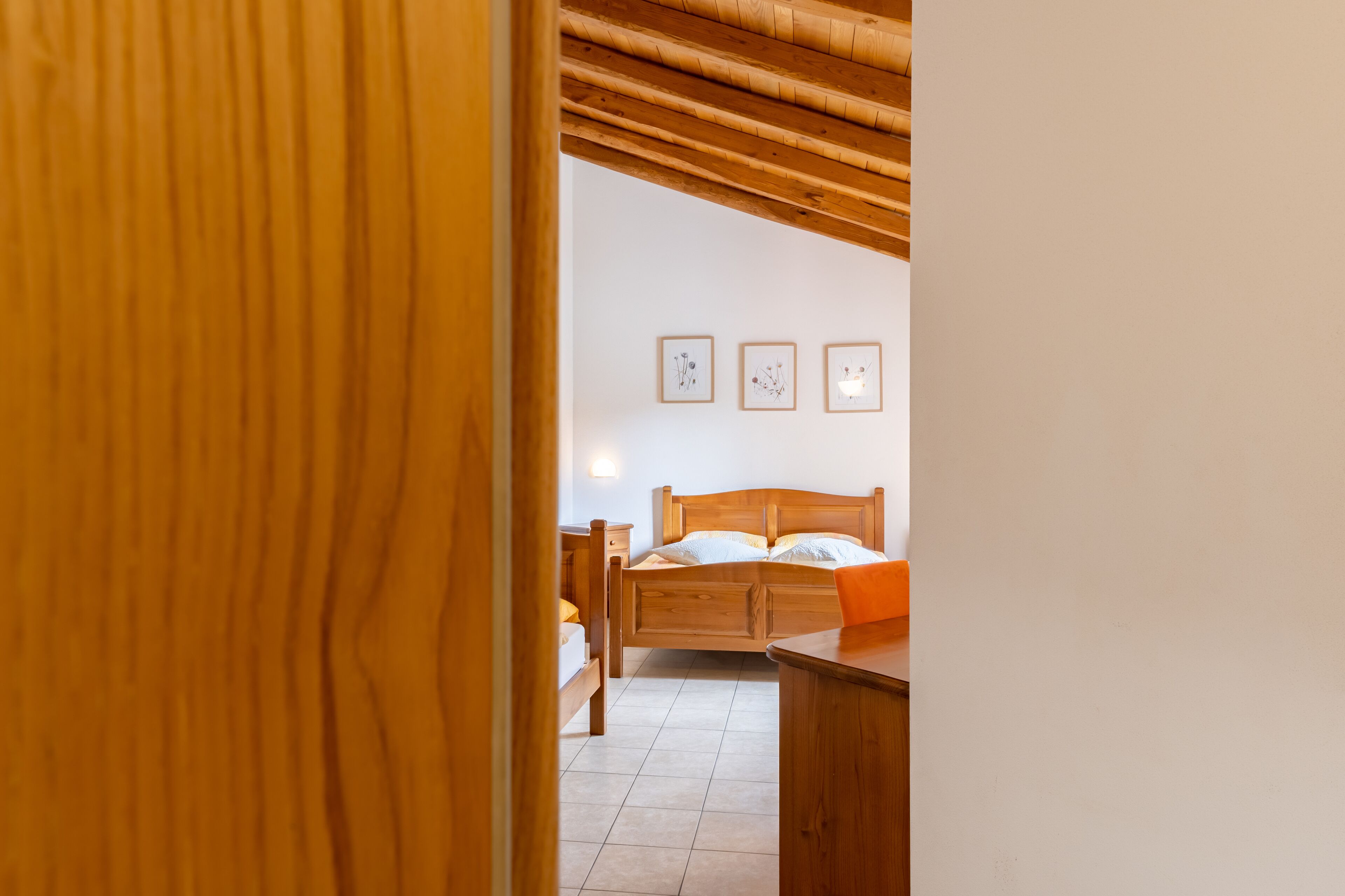 A wooden-framed room with a bed, a desk, and a chair. There are three framed pictures on the wall.