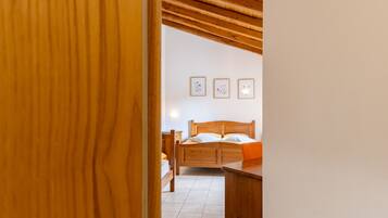A wooden-framed room with a bed, a desk, and a chair. There are three framed pictures on the wall.