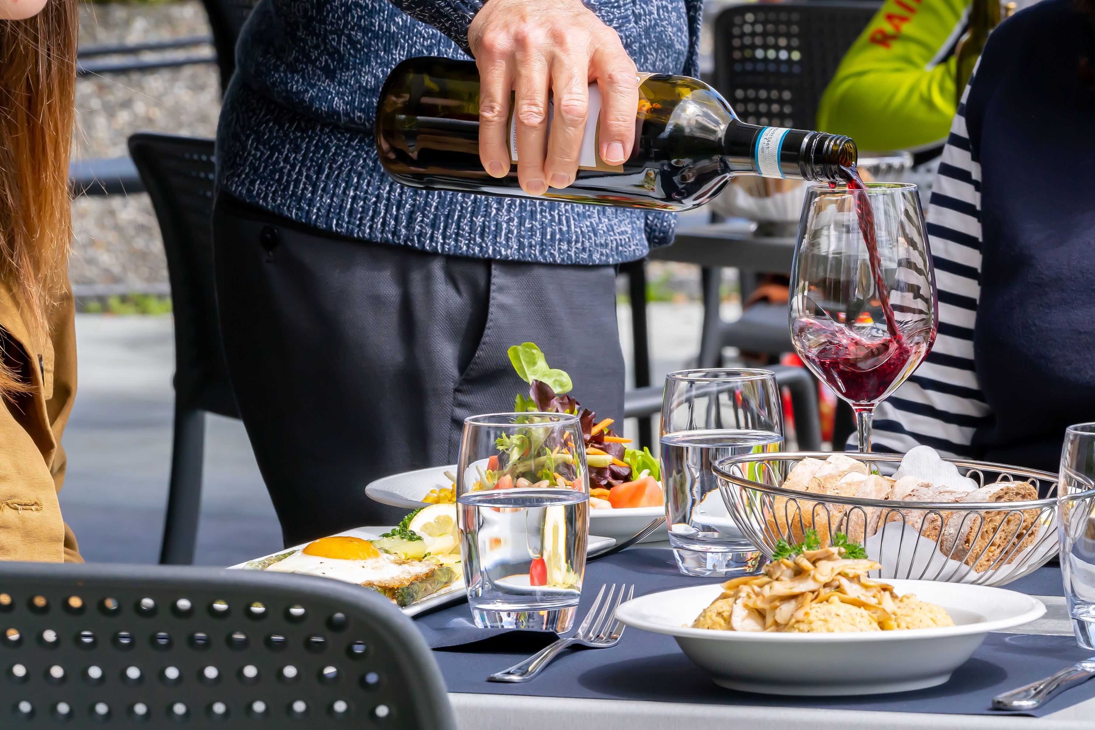 Mesa puesta con platos de comida, vasos y una botella de vino siendo servida.