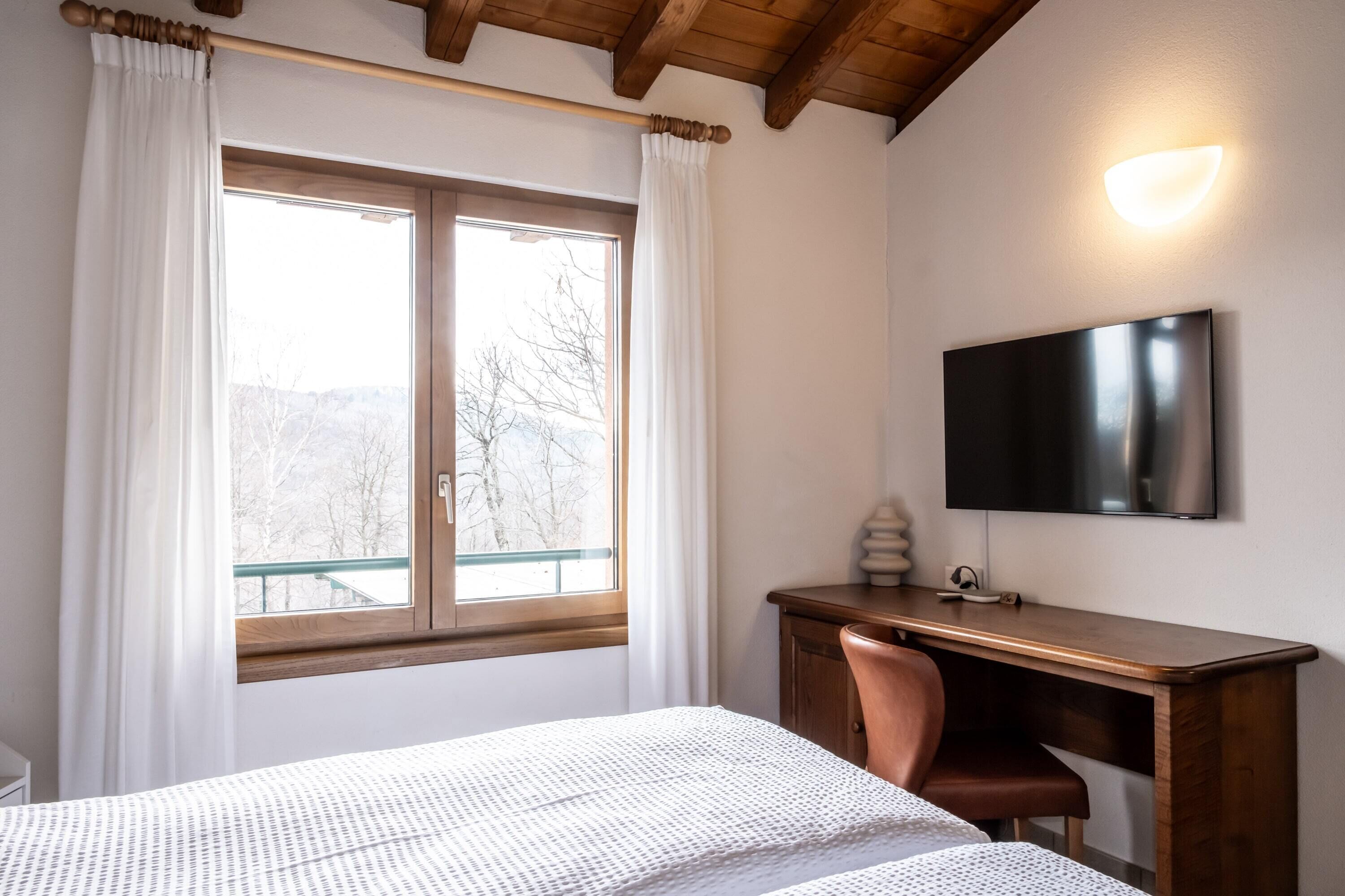 Une chambre à coucher avec un lit, un bureau, une chaise, une télévision et une fenêtre avec des rideaux.