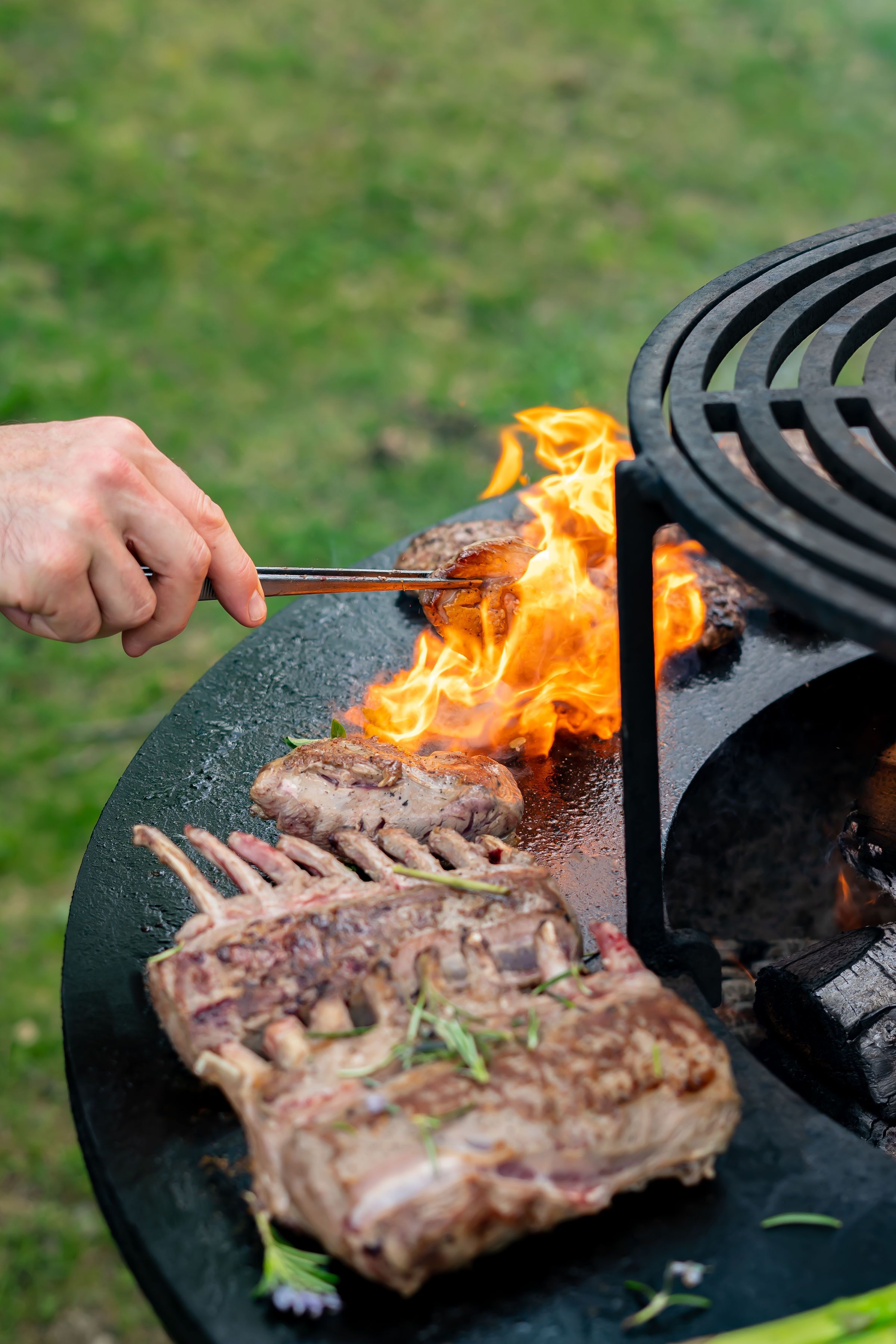 A person grilling meat on an outdoor grill with flames.