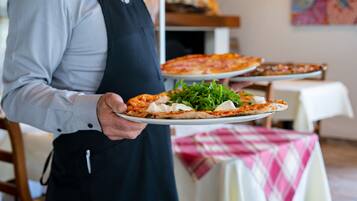 Une personne tenant une pizza sur une assiette blanche, avec une autre pizza sur un plateau en arrière-plan.
