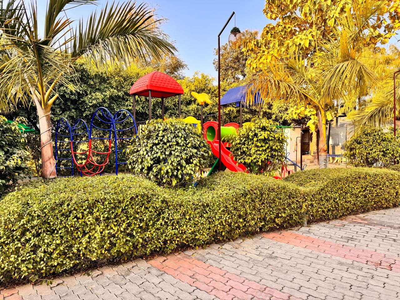 Un jardín ajardinado con un camino pavimentado, un tobogán rojo y diversas estructuras de juego.