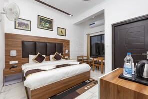 Ett modernt hotellrum med en sänggavel i trä, en säng med vita sängkläder, ett skrivbord med en vattenflaska och en dörr med ett handtag.