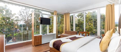 A modern hotel room with a large bed, a TV, a bedside phone, and a view of greenery through large windows.