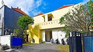 A residential building with a yellow facade, a red-tiled roof, and a gated entrance with parked motorcycles. - Hotel O Sandat Guest House (Denpasar)
