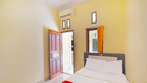 A hotel room with a bed, a window with curtains, an air conditioning unit, and a door. - Hotel O Sandat Guest House (Denpasar)