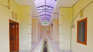 A corridor with a central walkway, flanked by doors and windows, leading to a room with a view of the sky through a translucent ceiling. - Hotel O Sandat Guest House (Denpasar)