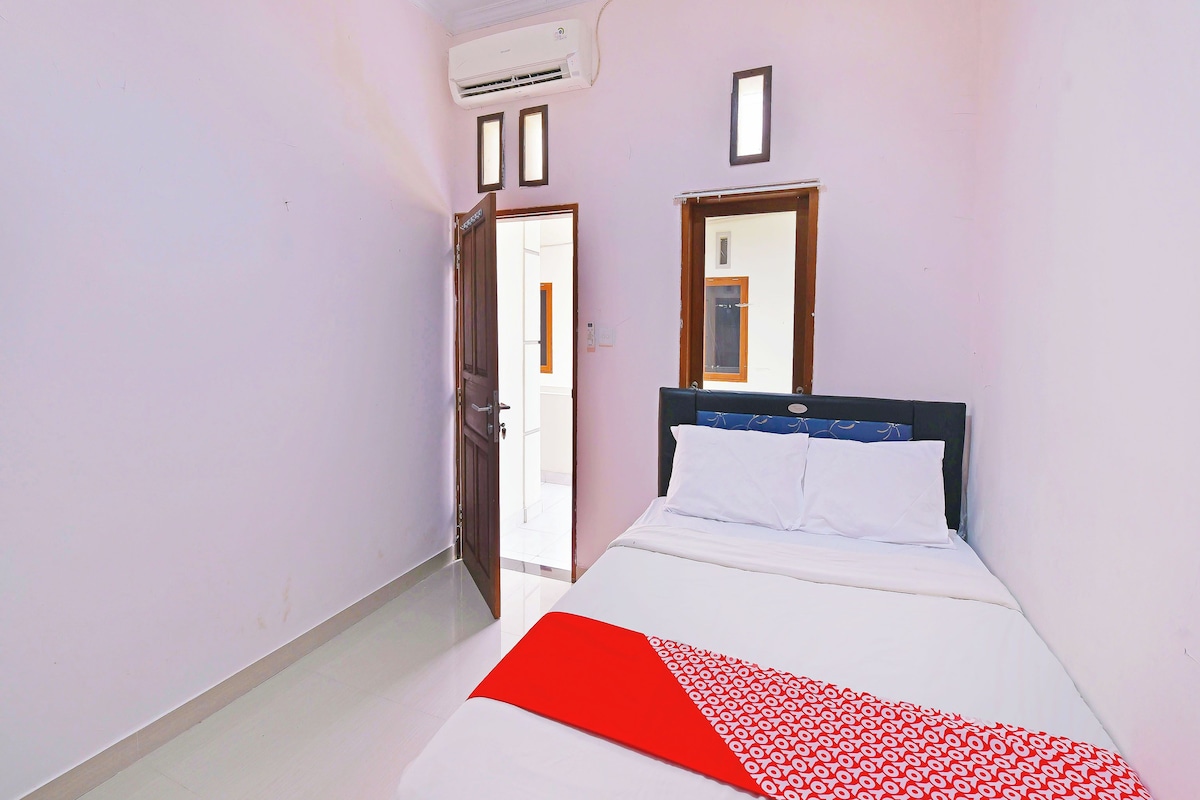 Ein schmales Hotelzimmer mit Bett, Fenster und Klimaanlage.