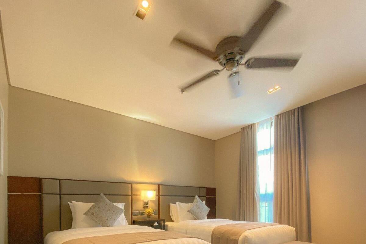 A hotel room with two beds, a ceiling fan, a nightstand with a lamp, and a window with curtains.