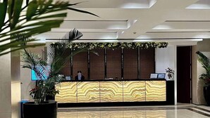 A modern reception area with a marble floor, a reception desk with a wood grain design, and potted plants.