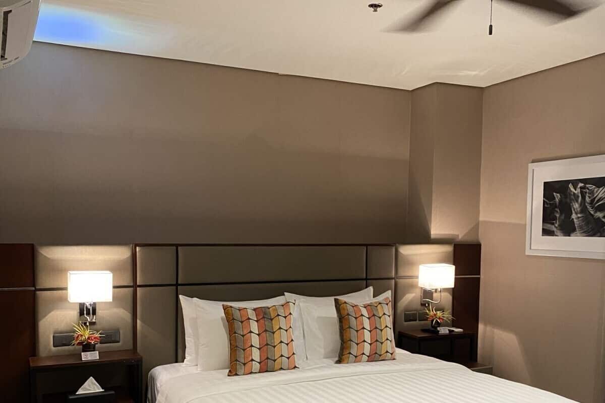 A hotel room with a large bed, two bedside tables with lamps, a ceiling fan, and a framed picture on the wall.
