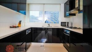 Uma cozinha moderna com armários pretos, bancada branca e janela com vista para edifícios.