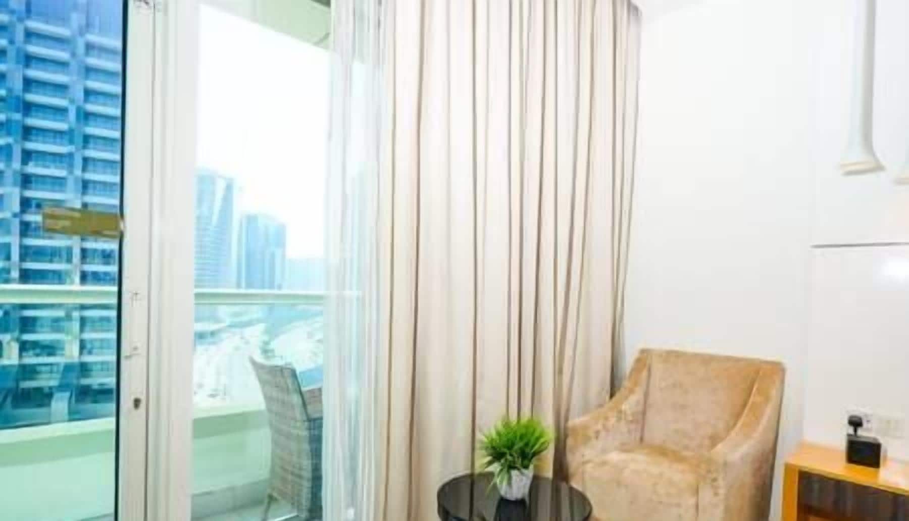 Une chambre d’hôtel moderne avec une grande fenêtre, un fauteuil confortable, une petite table avec une plante et une vue sur le paysage urbain.