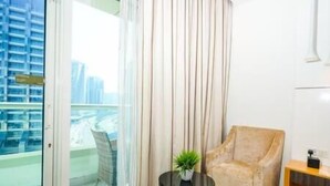 Quarto de hotel moderno com uma janela ampla, uma poltrona confortável, uma mesinha com uma planta e vista para a cidade.
