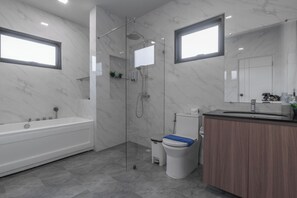 Un baño moderno con ducha de vidrio, bañera, inodoro y tocador con espejo.