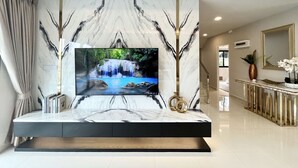 A modern living room with a large flat-screen TV mounted on a marble wall, a minimalist console table, and a staircase leading to another level. - Southern Peak Pool Villa HuayYai Pattaya (Sattahip)