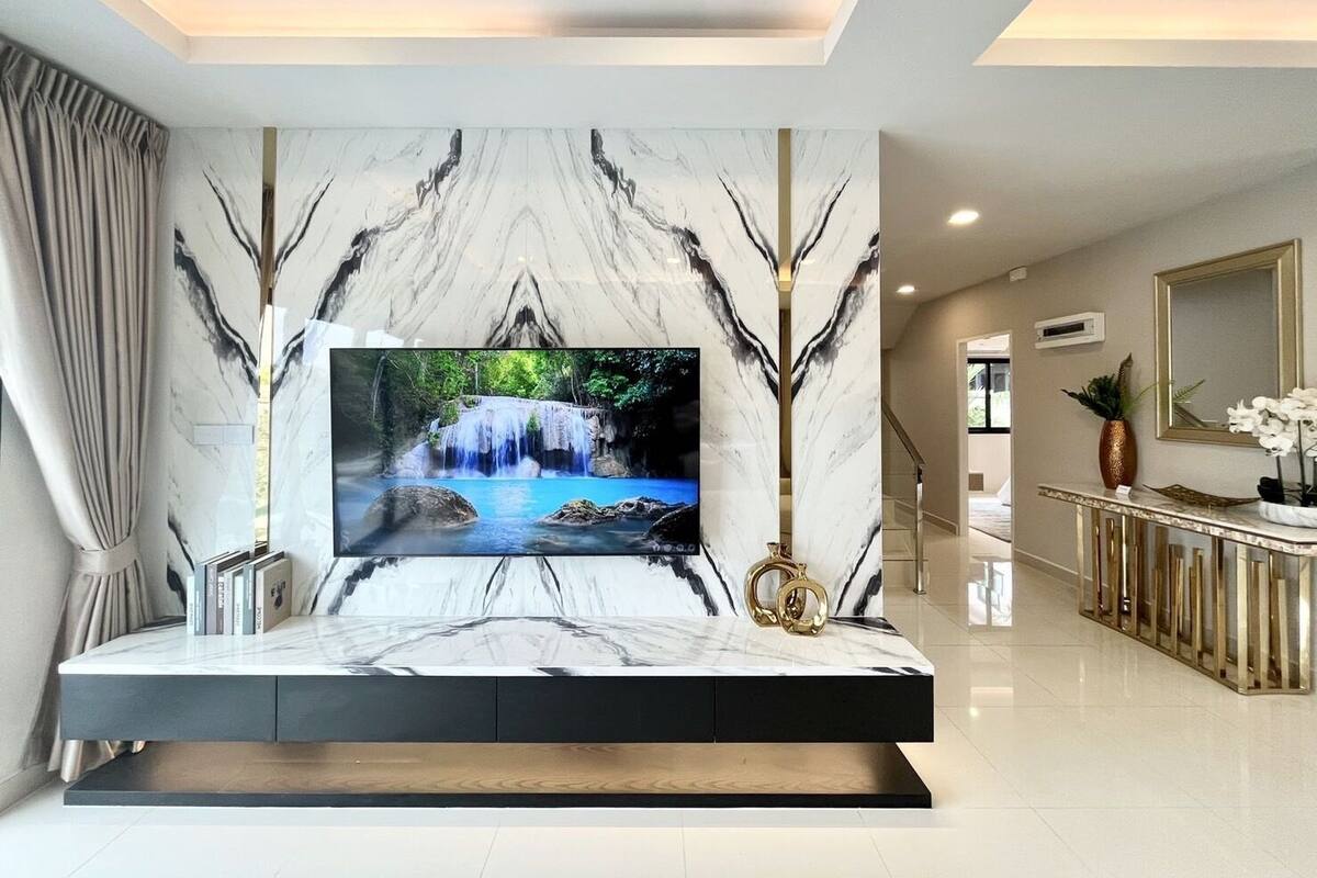 Una sala de estar moderna con un televisor de pantalla plana grande montado en una pared de mármol, una consola minimalista y una escalera que conduce a otro nivel.