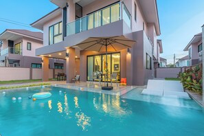 Un moderno edificio residencial de dos pisos con piscina, mobiliario exterior y un patio cubierto.