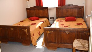 A double bed with floral bedding and red pillows, a wooden chair, and a radiator. - Beautiful T3 apartment with balcony and magnificent view (Font-Romeu-Odeillo-Via)