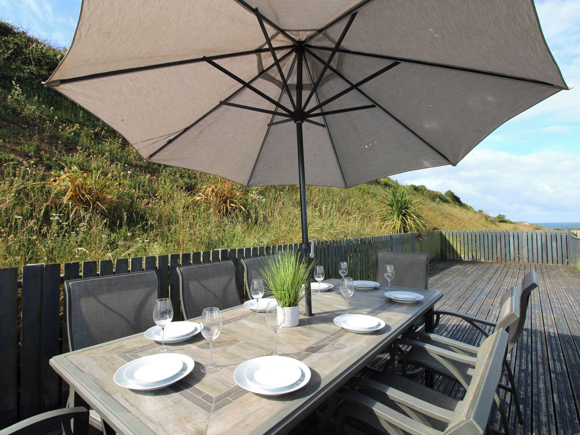 Un área de comedor al aire libre con una mesa lista para cuatro personas, una sombrilla y sillas.