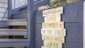 En träskylt med texten ”Lite sand mellan tårna får alltid en att må bättre” är upphängd på en vägg.