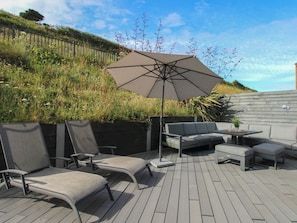 An outdoor patio with a grey sofa, two lounge chairs, a table, and a large umbrella. - 7 Beachdown (Kingsbridge)