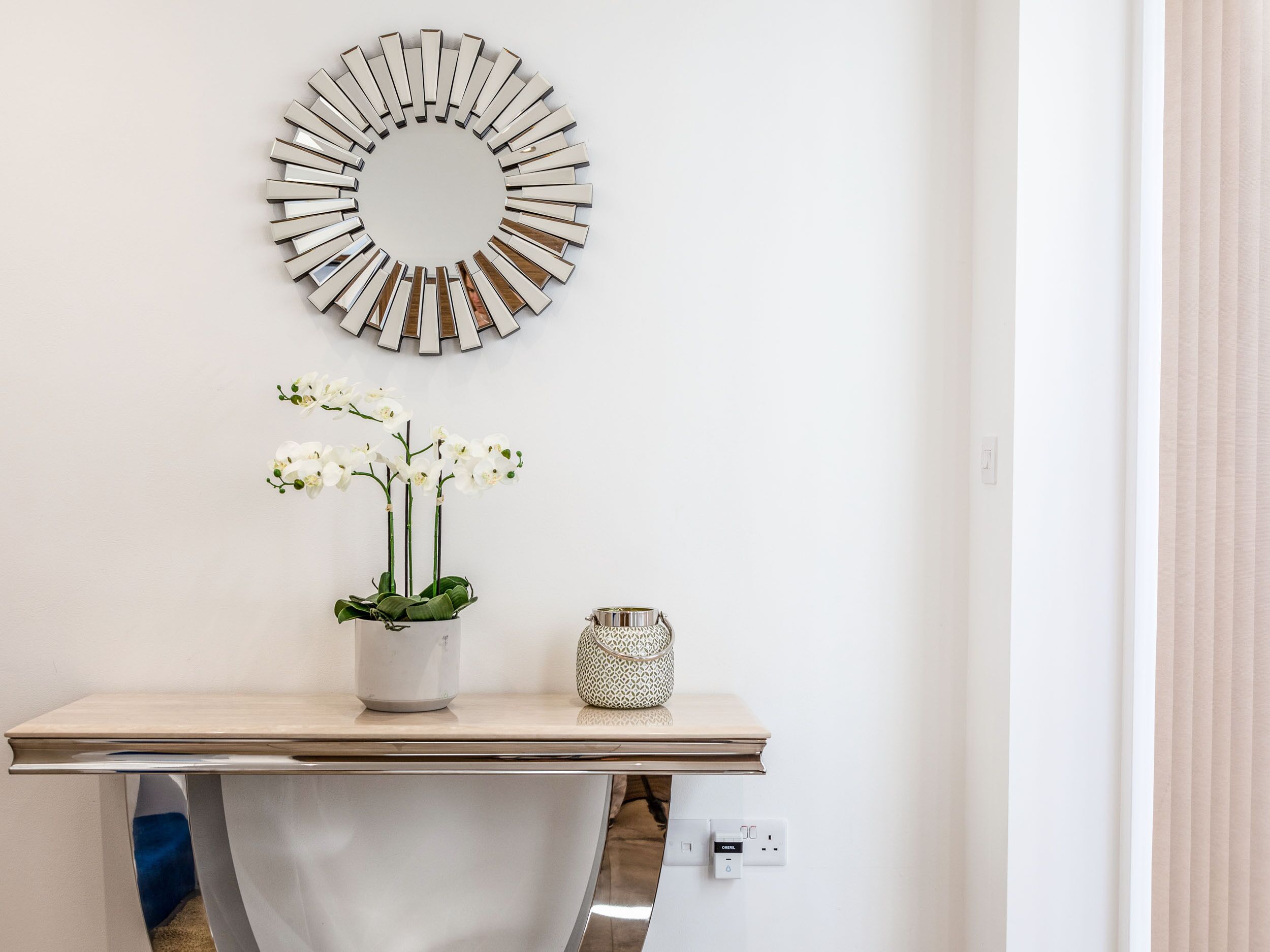 A bathroom with a white sink, a mirror, a vase with white flowers, and a patterned container.