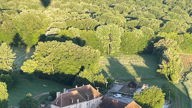 Vista aèria d'una extensa propietat amb diversos edificis, camps verds extensos i un bosc dens al fons.
