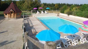 Una piscina amb gandules i ombrel·les, una cabana de fusta i un bosc al fons.