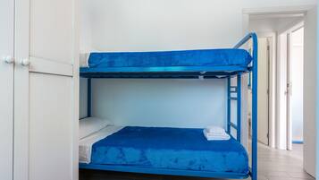 A bunk bed with a blue mattress and white pillows, a white wardrobe, and a wooden floor.