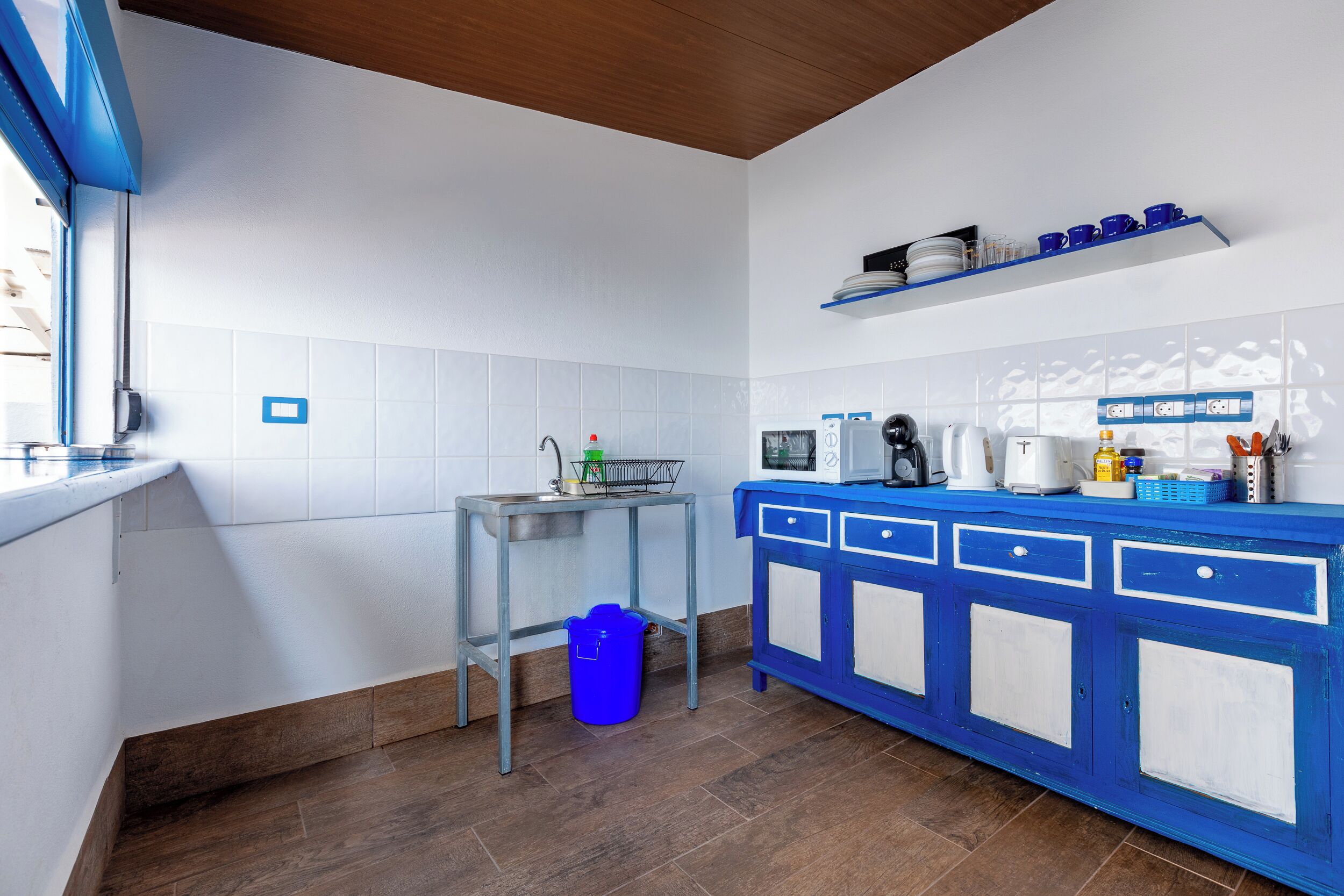 A modern kitchen with a blue and white color scheme, featuring a stainless steel countertop, a microwave, and a coffee maker.