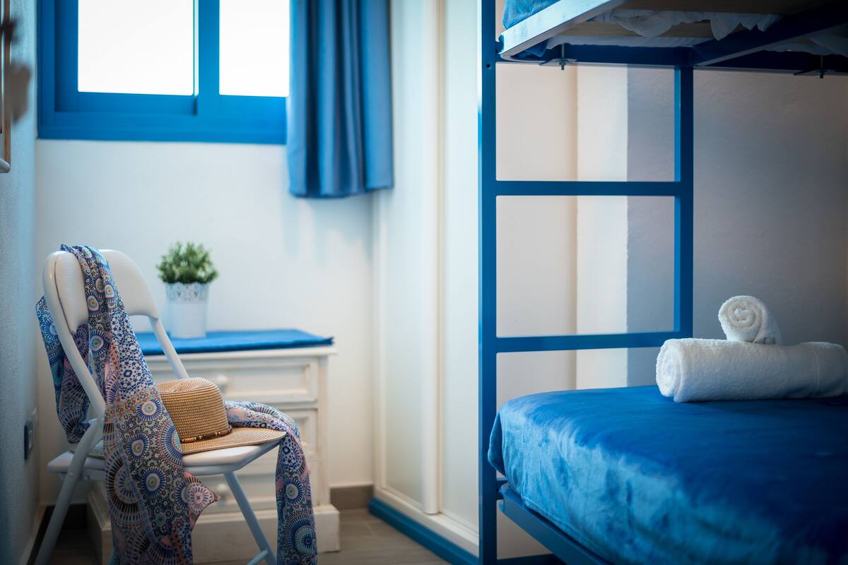 Een kamer met een stapelbed, een stoel met een gestreept kussen, en een kleine plant in een pot.