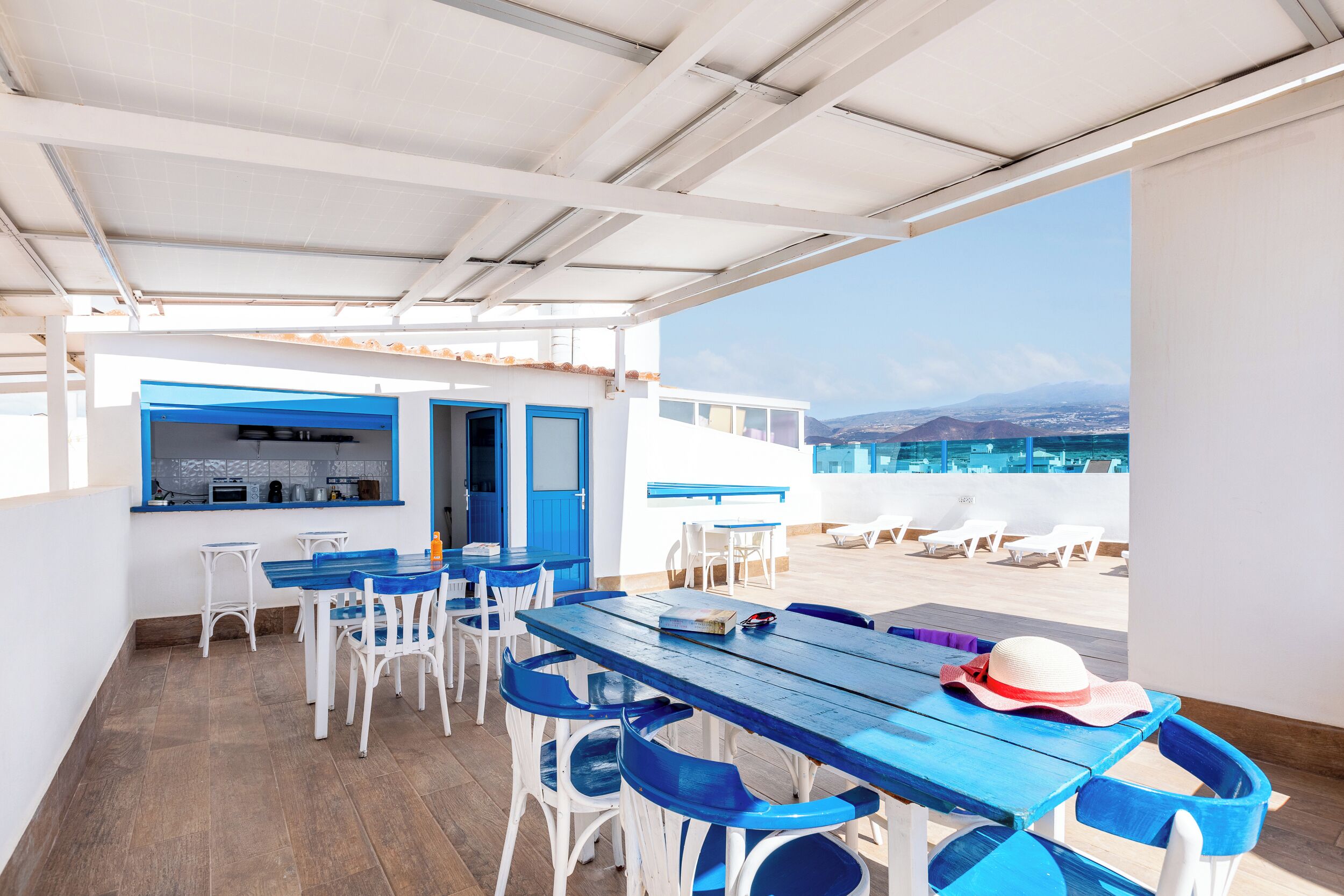 A rooftop terrace with blue and white furniture, a view of the sea, and a bar area with a blue door.