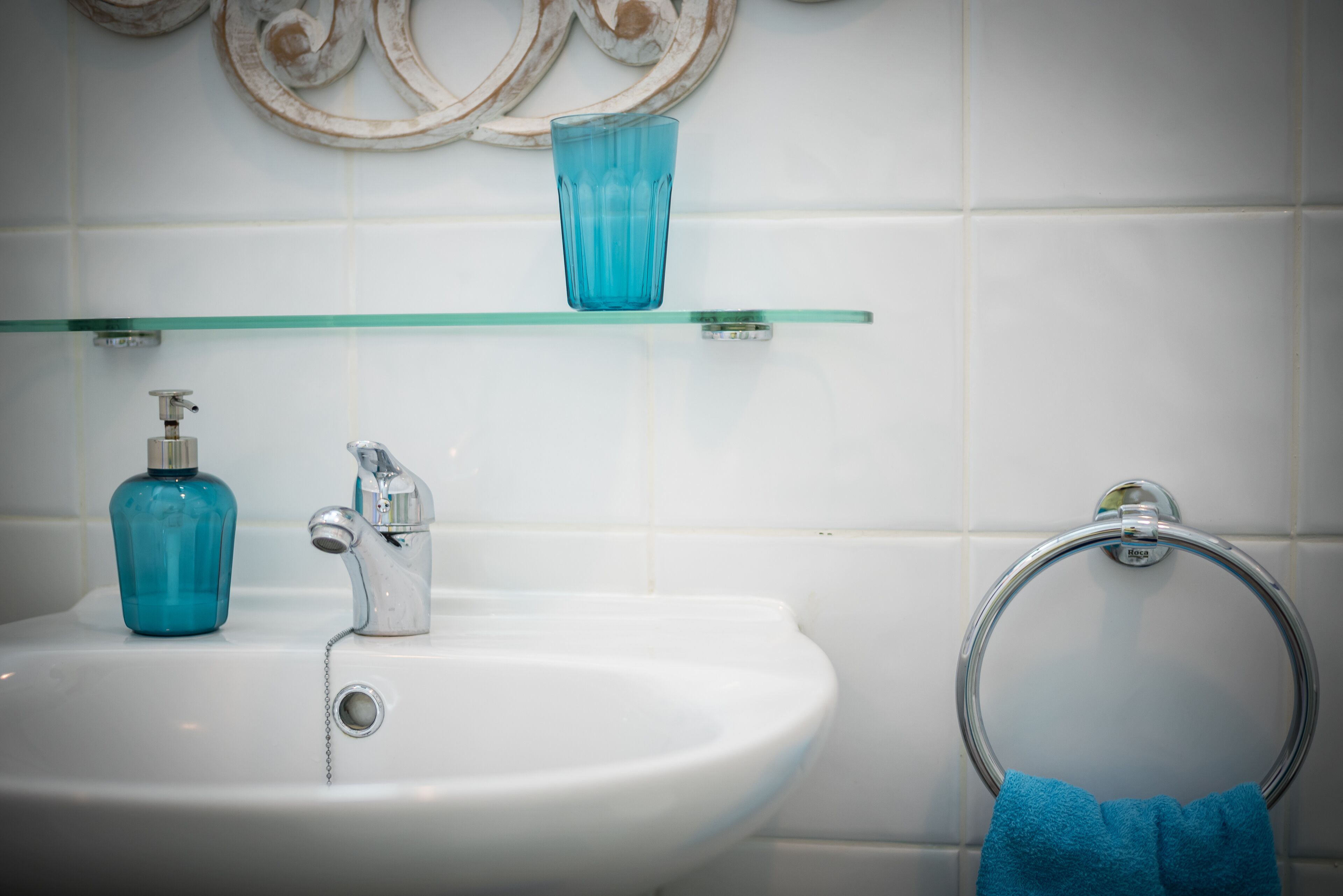 Ein Badezimmer mit einem weißen Waschbecken, einer blauen Glasflasche und einem Handtuchhalter.