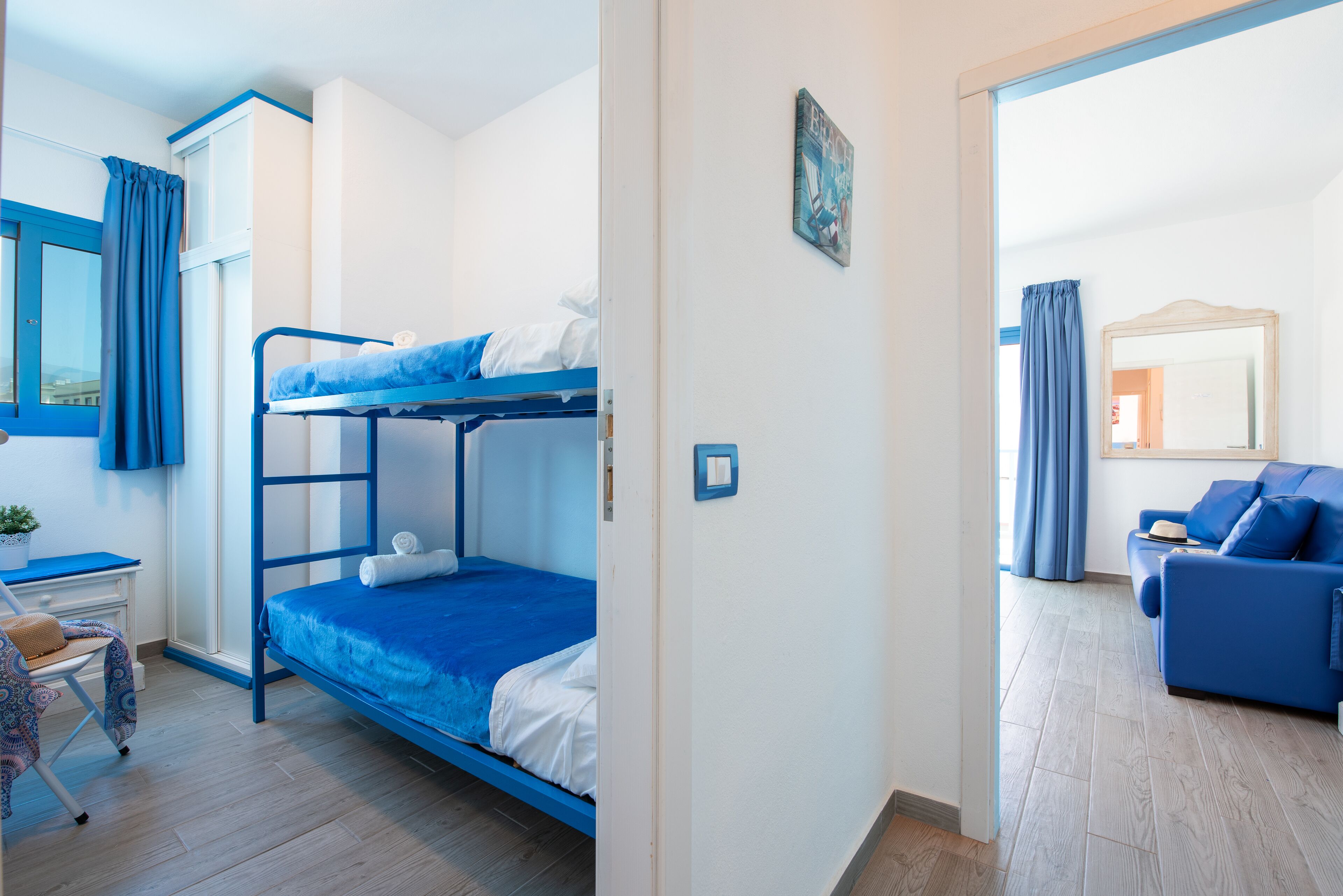 A room with a bunk bed, a desk with a chair, a sofa, and a mirror.