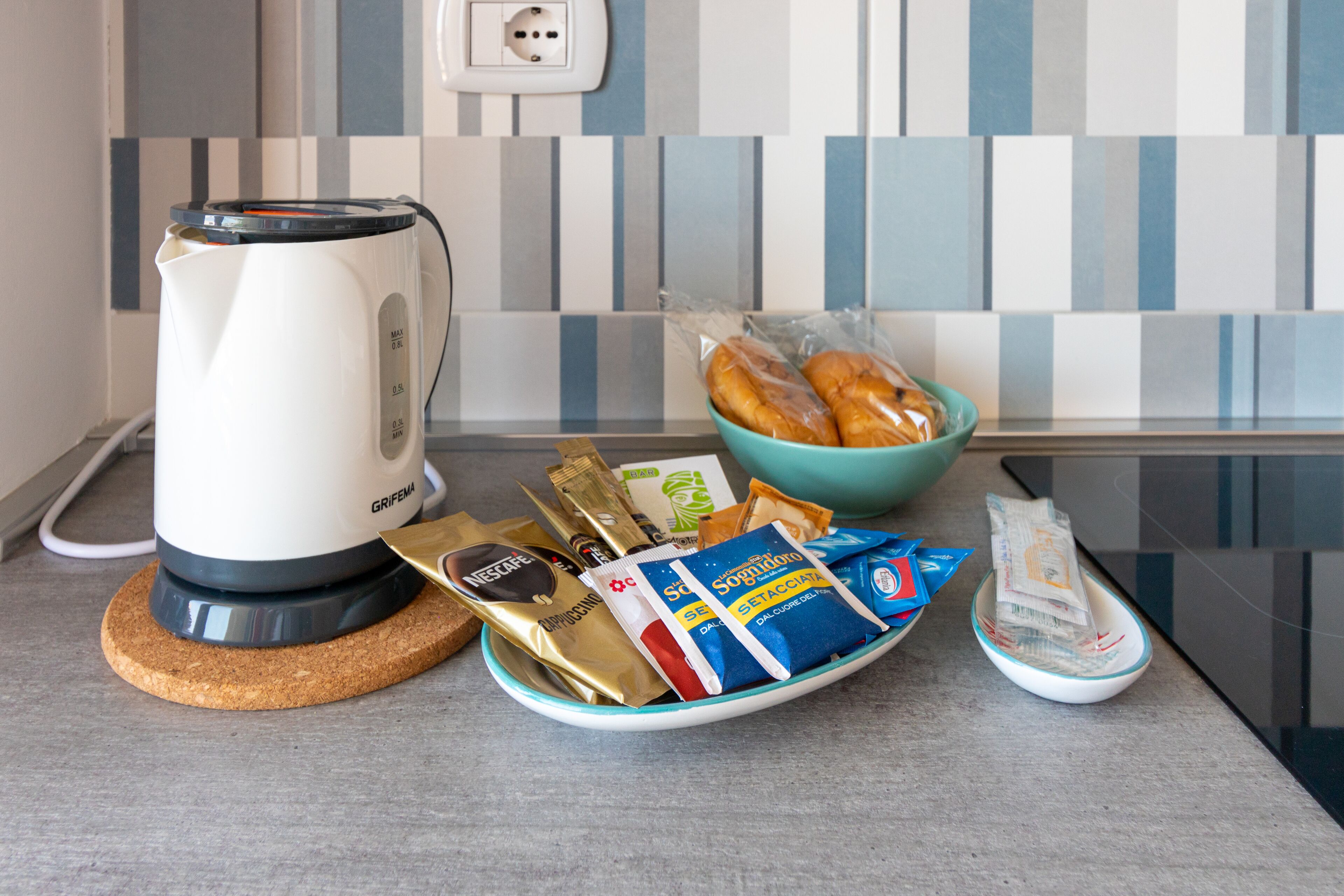 Una encimera de cocina con una cafetera, un bol de pan y diferentes productos de snack envasados.