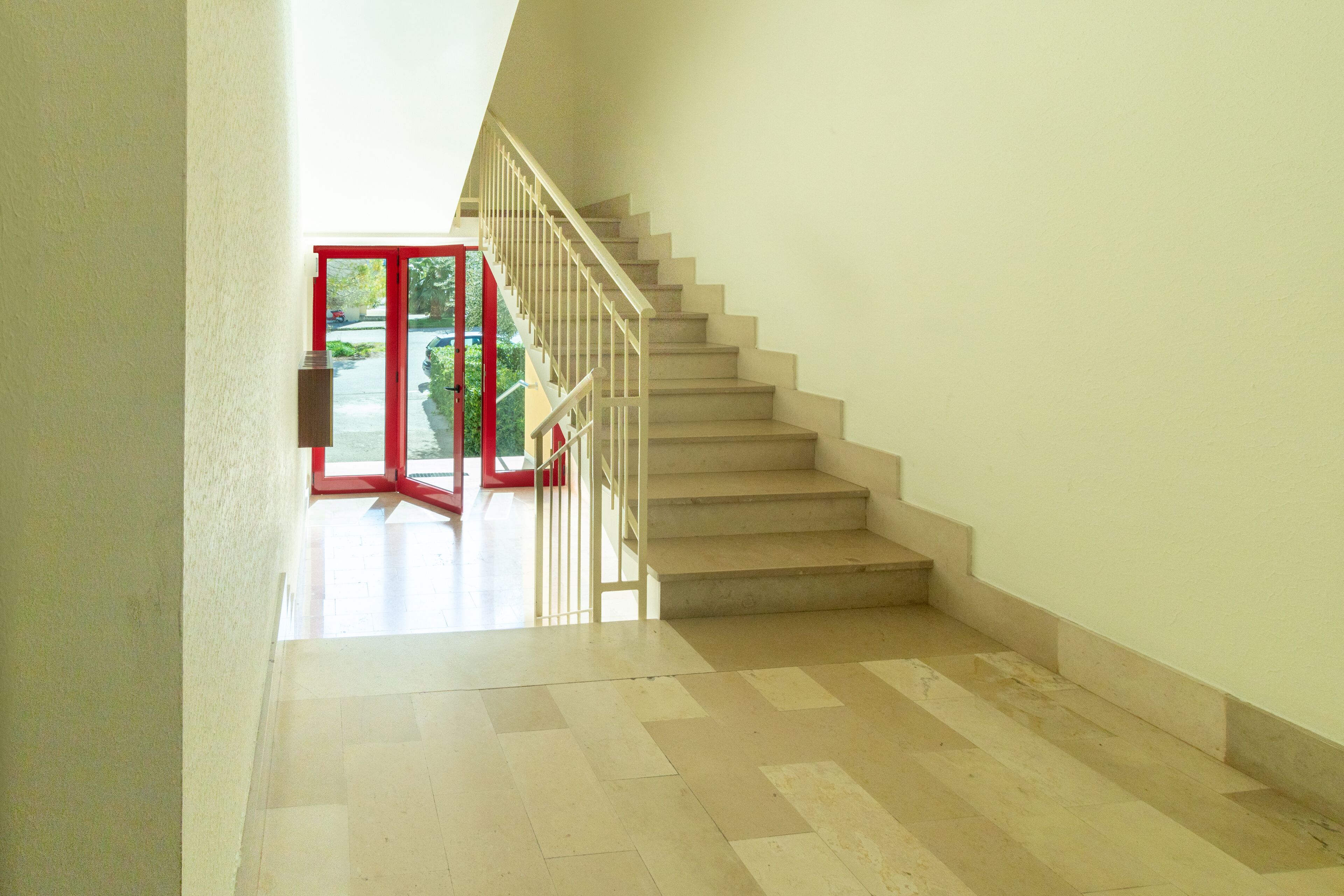 Una escalera con barandilla roja que lleva a una puerta abierta.