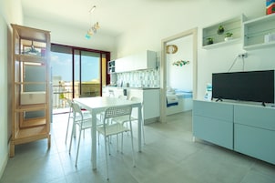 A modern kitchen with white cabinets, a dining table with chairs, and a TV on a cabinet.