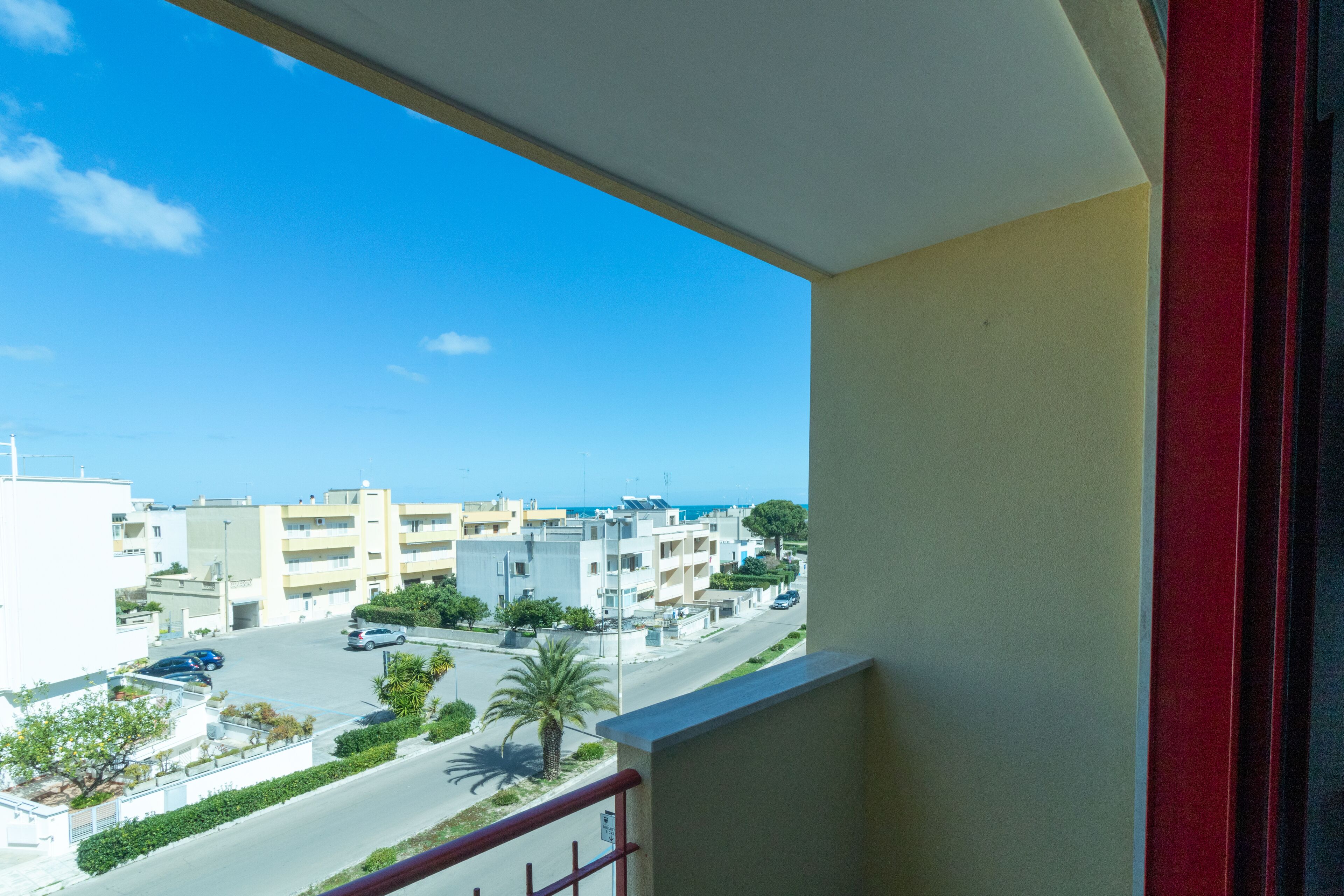 A balcony with a view of a coastal street, buildings, and a clear blue sky.