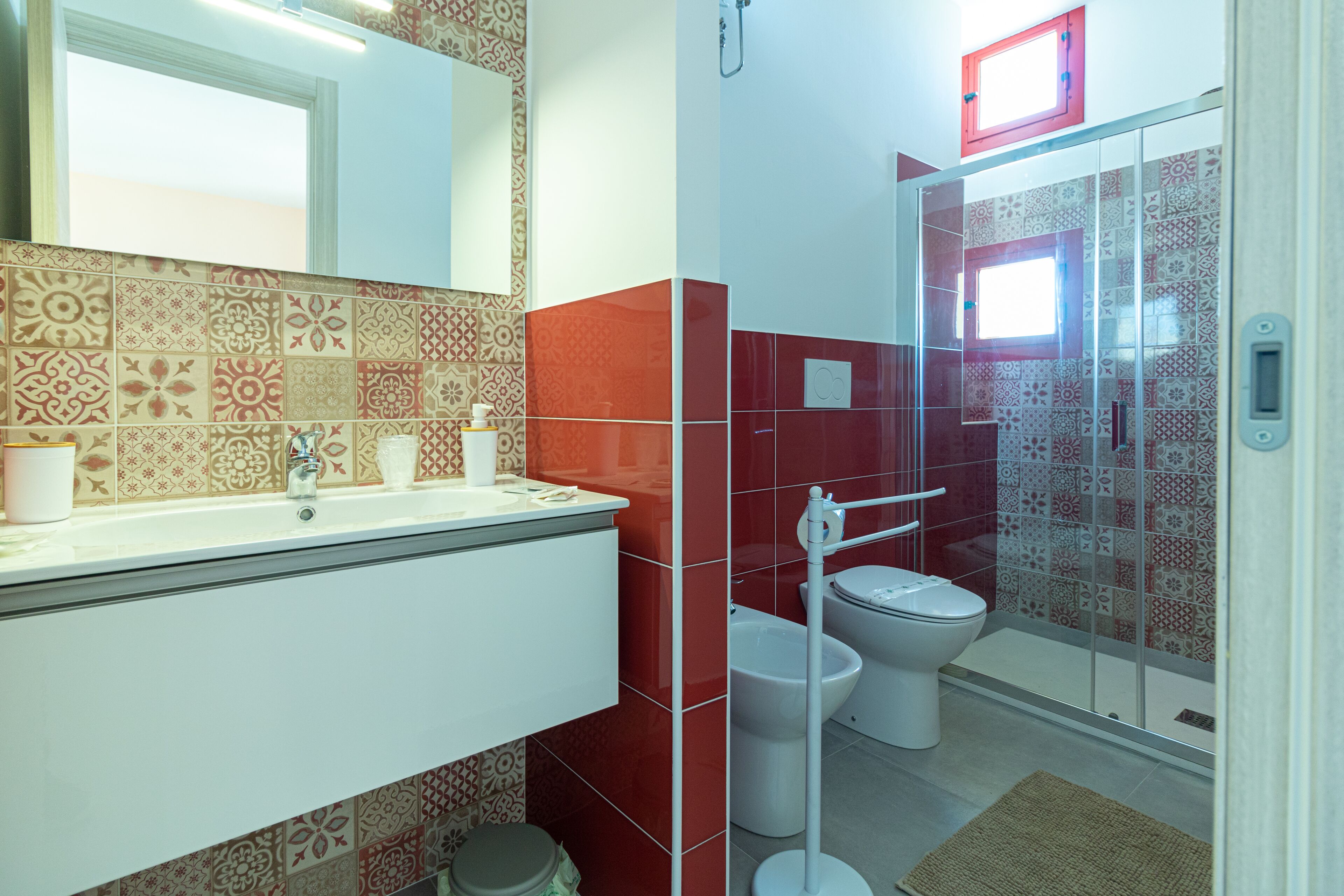 Une salle de bain avec un mur recouvert de carreaux décoratifs, un lavabo blanc et une douche à paroi de verre.