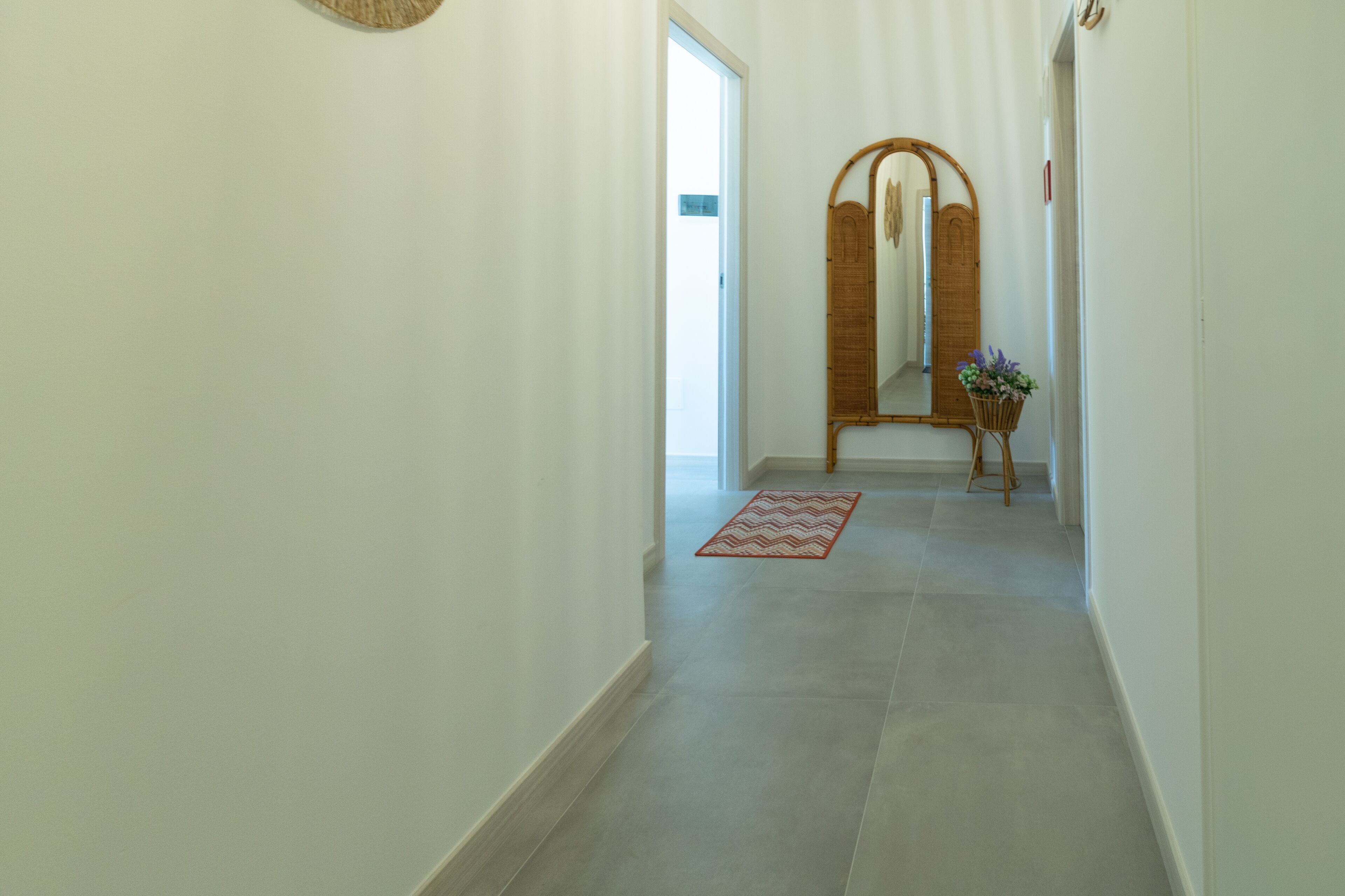 A hallway with a large mirror, a small plant, and a red patterned rug.
