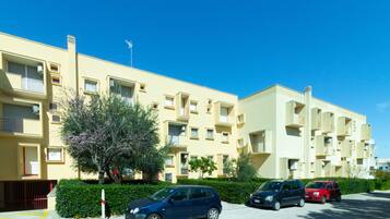 Un edificio residencial de varios pisos con balcones, un estacionamiento y un cielo azul despejado.