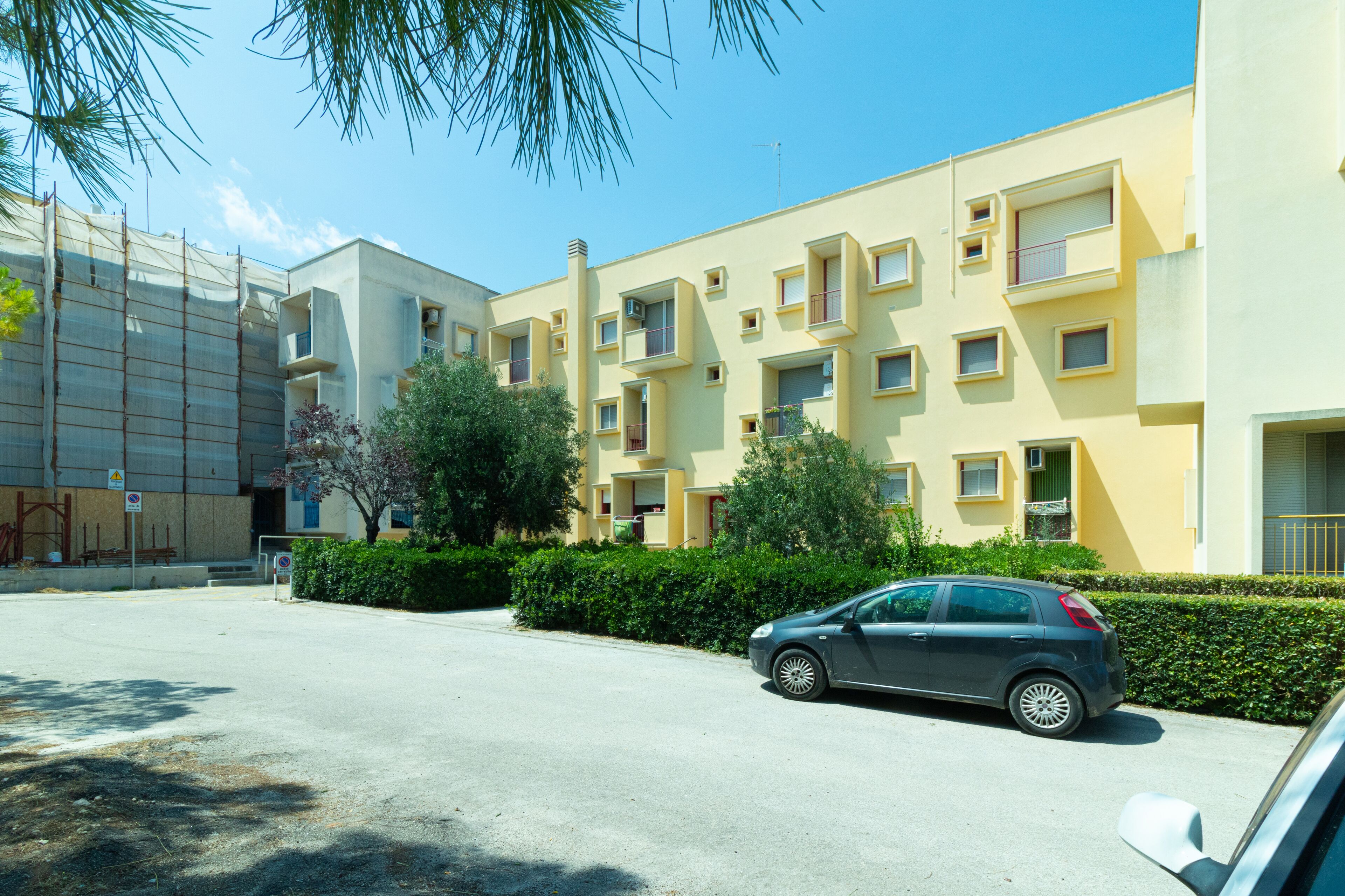Un edificio de apartamentos moderno con varios balcones y un coche estacionado frente a él.