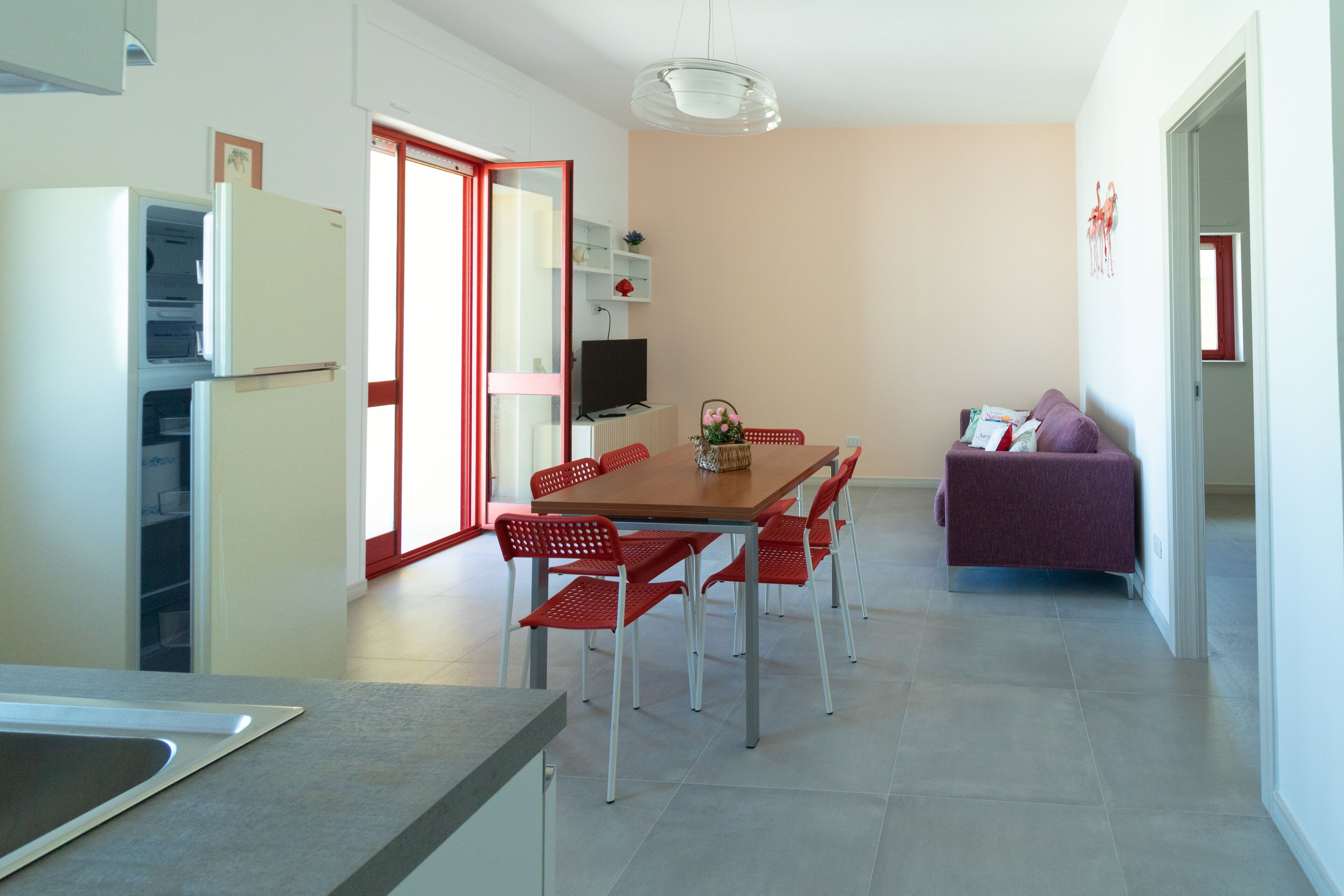 A modern kitchen with a dining area, a TV, and a sofa.