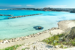 Une vue sur la côte, avec une eau turquoise limpide, un rivage rocheux et des bâtiments qui se dessinent à l’horizon.