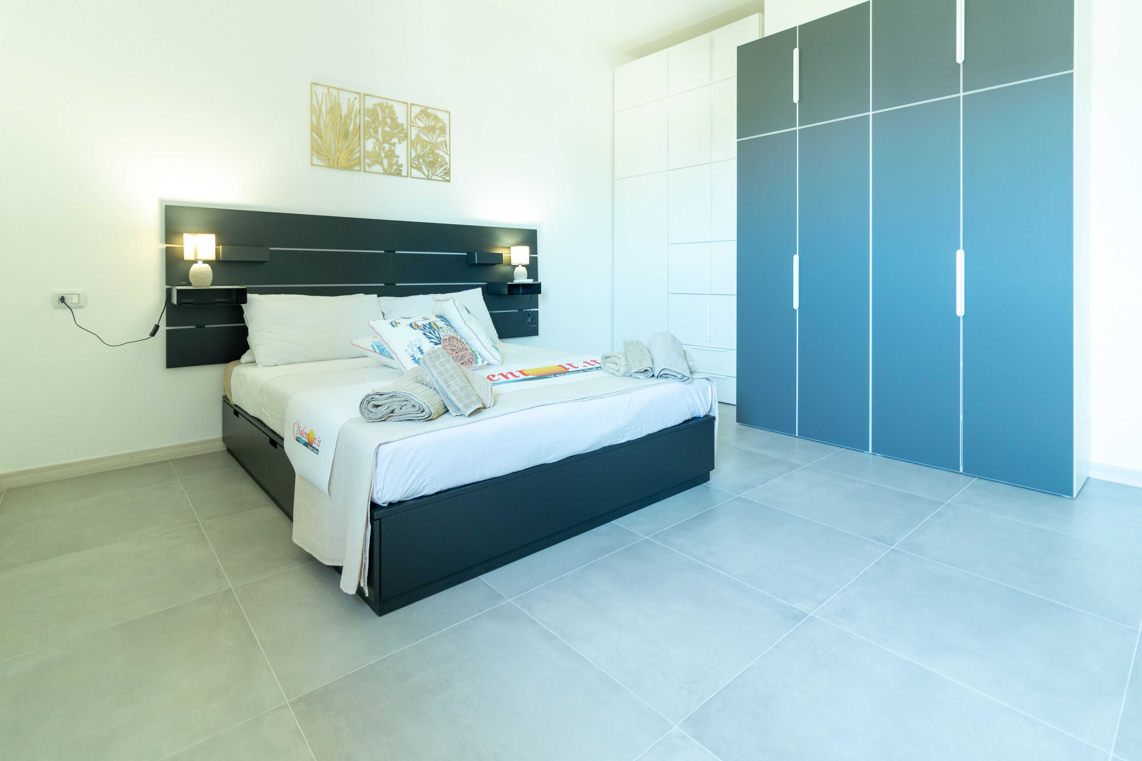 Un dormitorio moderno con una cama, lámparas de noche, un armario y una obra de arte colgada en la pared.